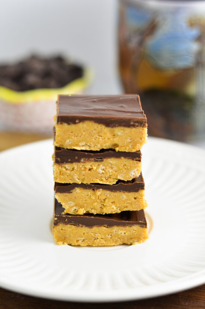 A stack of Chocolate Peanut Butter Squares on a small plate with semisweet chocolate chips in the background.