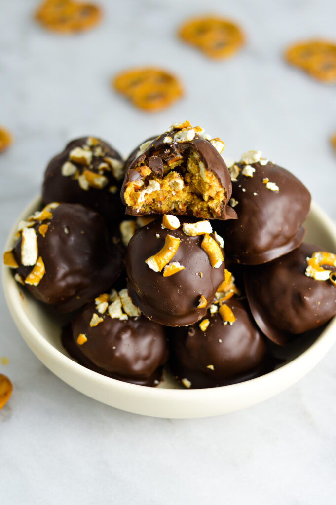 A bowl with Chubby Hubby truffles with a bite taken out of the top truffle surrounded by pretzels.