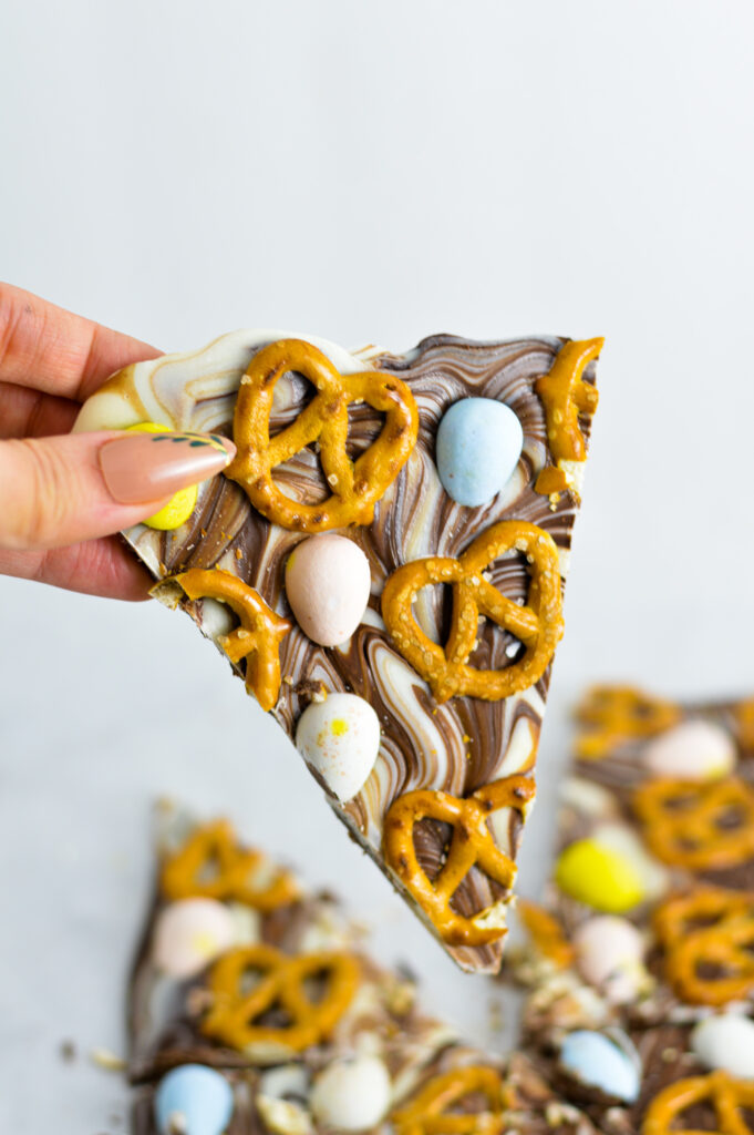 A hand holding a triangular slice of Chocolate swirled Easter Bark.