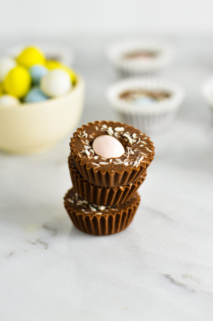 3 Easter Nest Nutella Cups stacked with a small bowl of Mini Eggs in the background.