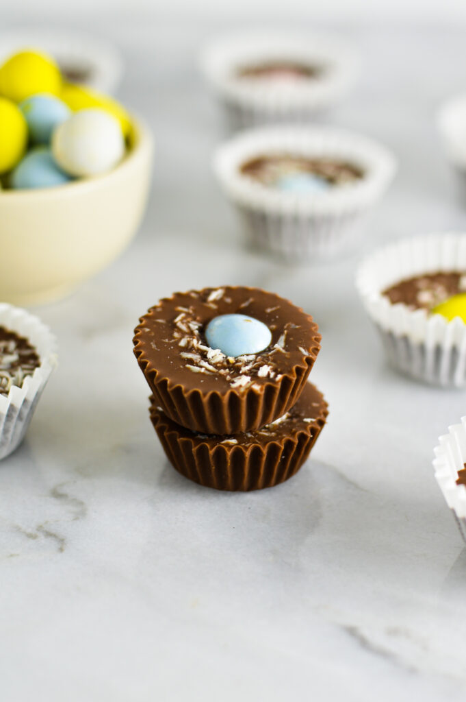 Two Easter Nest Nutella Cups with a small white bowl of multicolored Mini Eggs in the background.