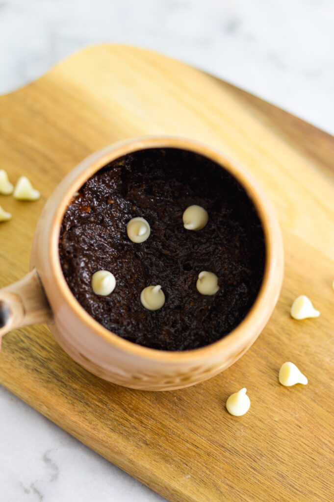 Overhead shot of a White Chocolate Nutella Mug Cake on a wooden cutting board.