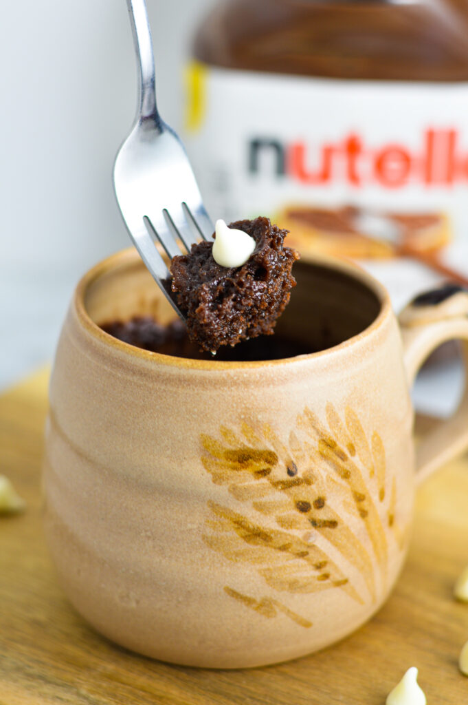 A forkful of White Chocolate Nutella Mug Cake with a jar of Nutella in the background.