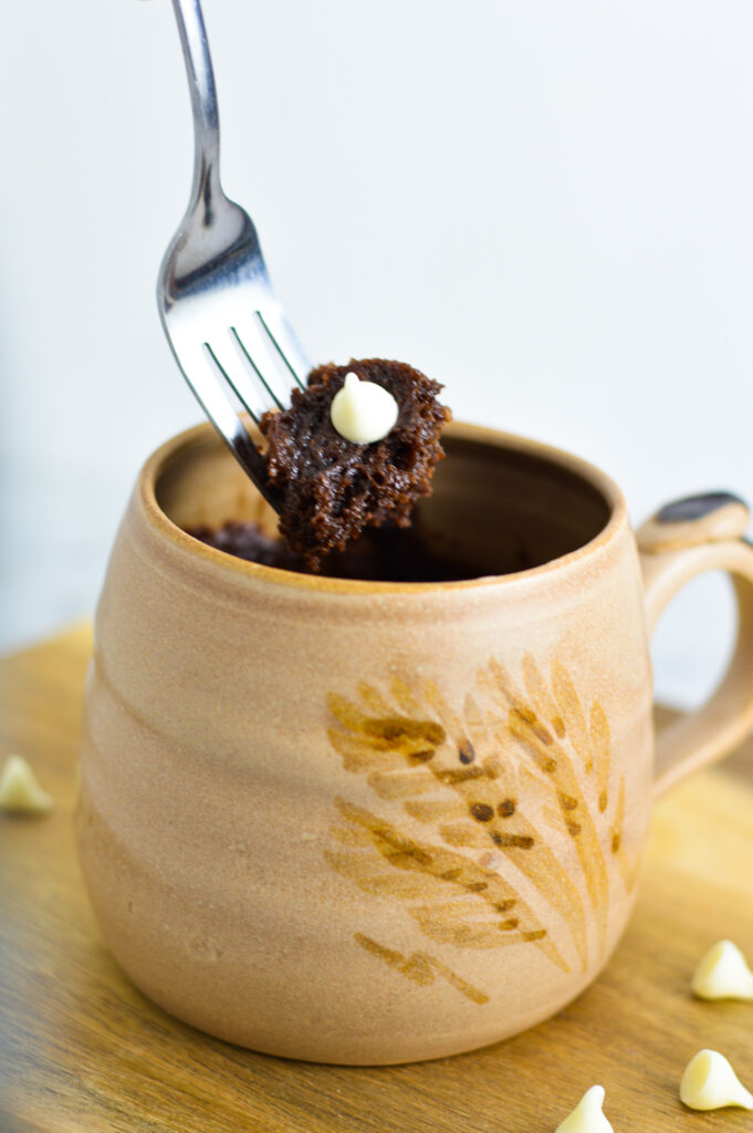 A fork digging into a Nutella mug cake with white chocolate chips.