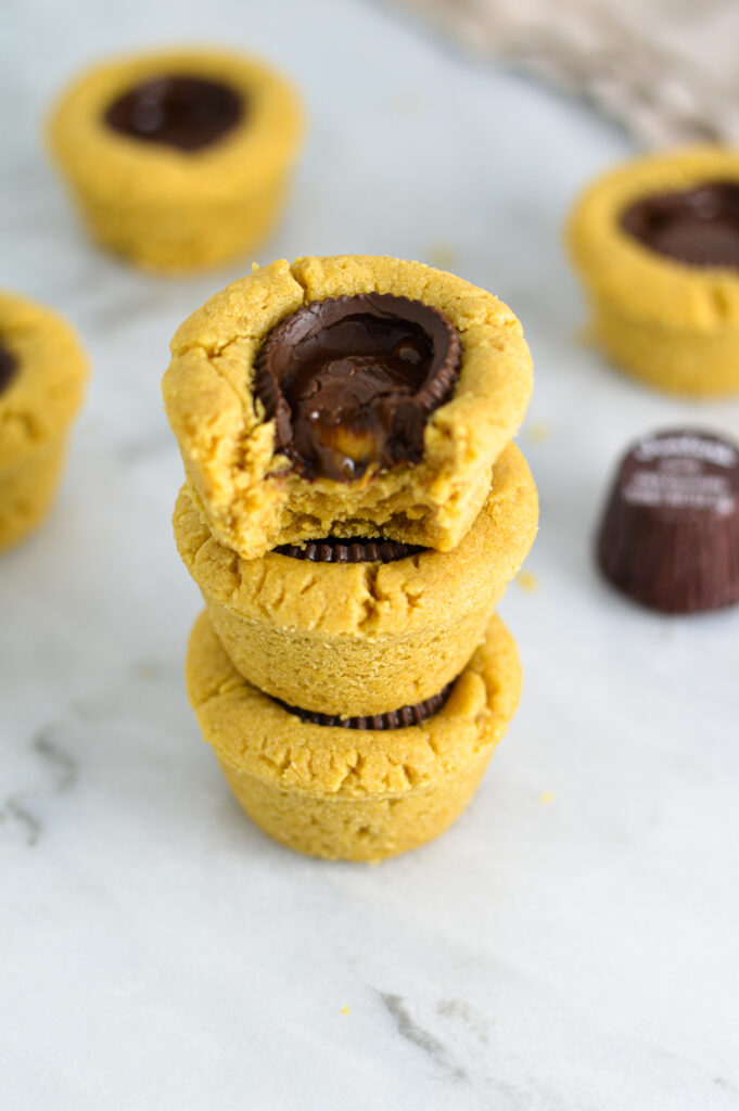 A closeup of a stack of Dark Chocolate Peanut Butter Cookie Cups with a bite taken out of the top cookie cup.