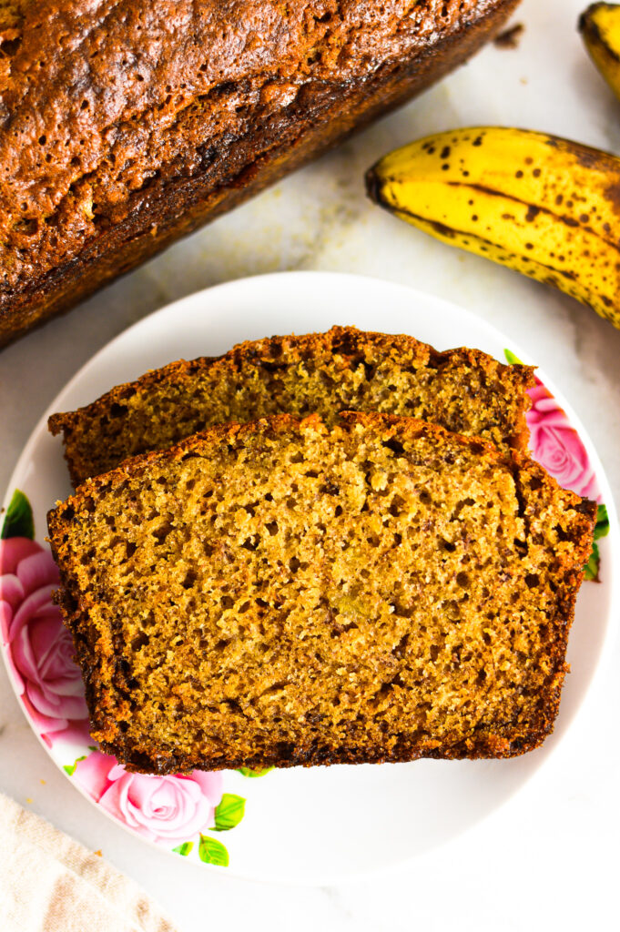 2 slices of Ginger Banana Bread on a white plate with brown spotted bananas beside it.