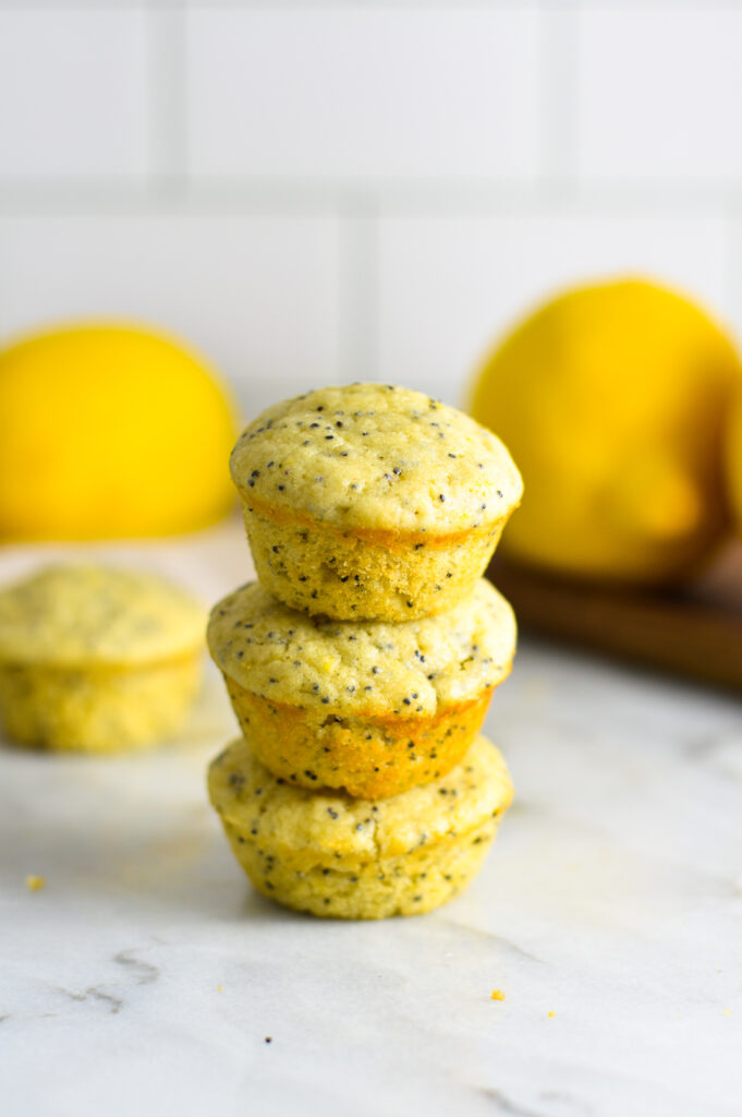 A stack of 3 Lemon Poppy Seed Mini Muffins with large yellow lemons in the background.