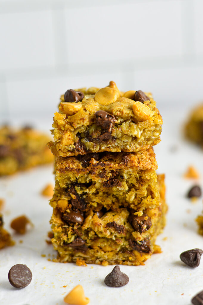 A stack of Oatmeal Butterscotch Chocolate Chip Cookie Bars with semi-sweet chocolate chips and butterscotch chips in the background.