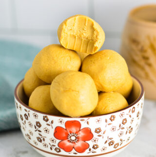 Peanut Butter Balls in a small bowl with a bite taken out of the top one and a coffee cup in the background.