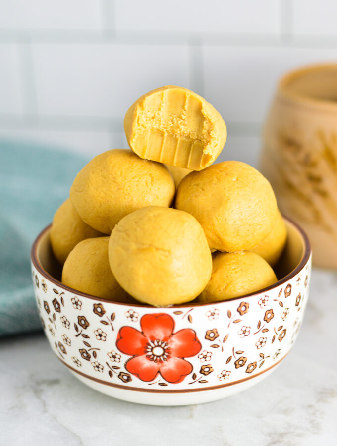 Peanut Butter Balls in a small bowl with a bite taken out of the top one and a coffee cup in the background.