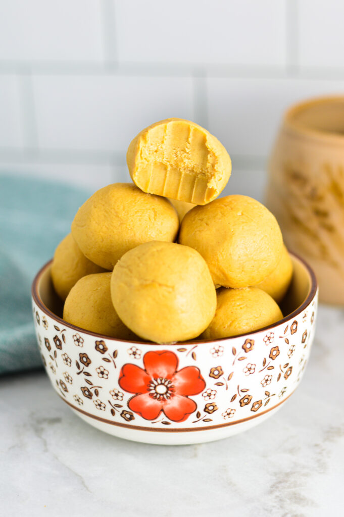 Peanut Butter Balls in a small bowl with a bite taken out of the top one and a coffee cup in the background.