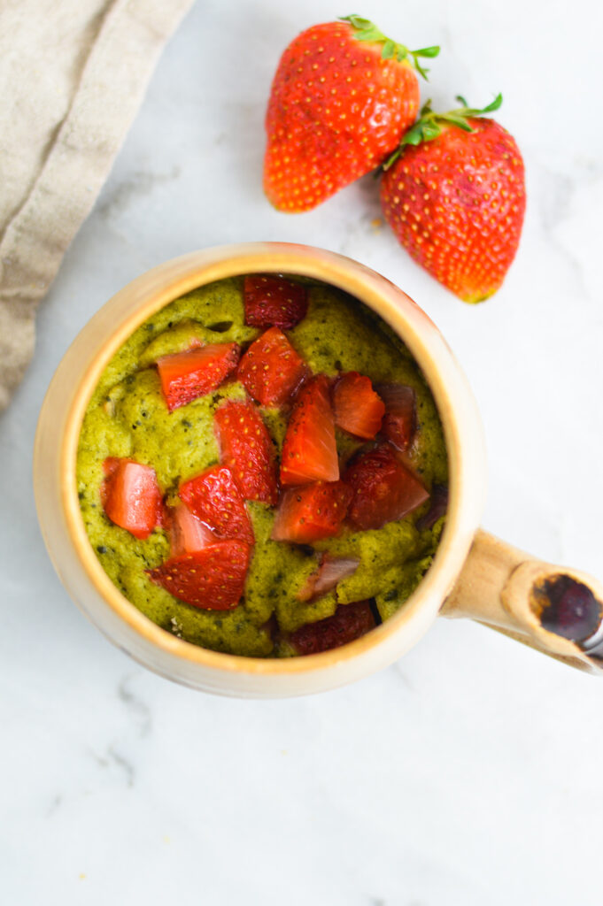 Overhead shot of a Matcha Mug Cake with fresh strawberries on top.