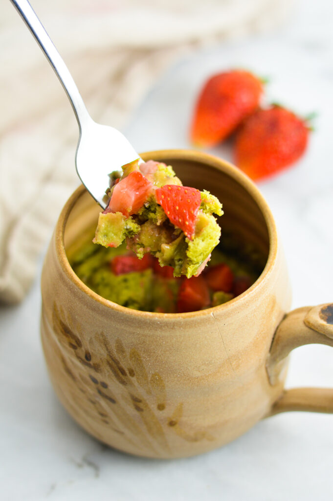 A bite of Strawberry Matcha Mug Cake taken from a tan ceramic mug.