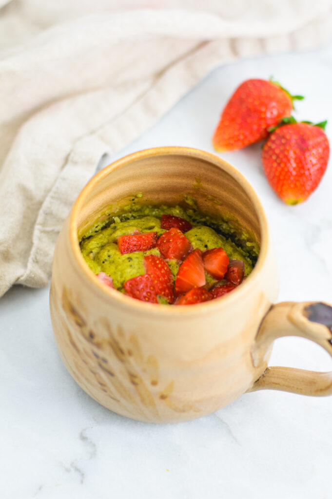 Strawberry Matcha Mug Cake with fresh strawberries in the background.