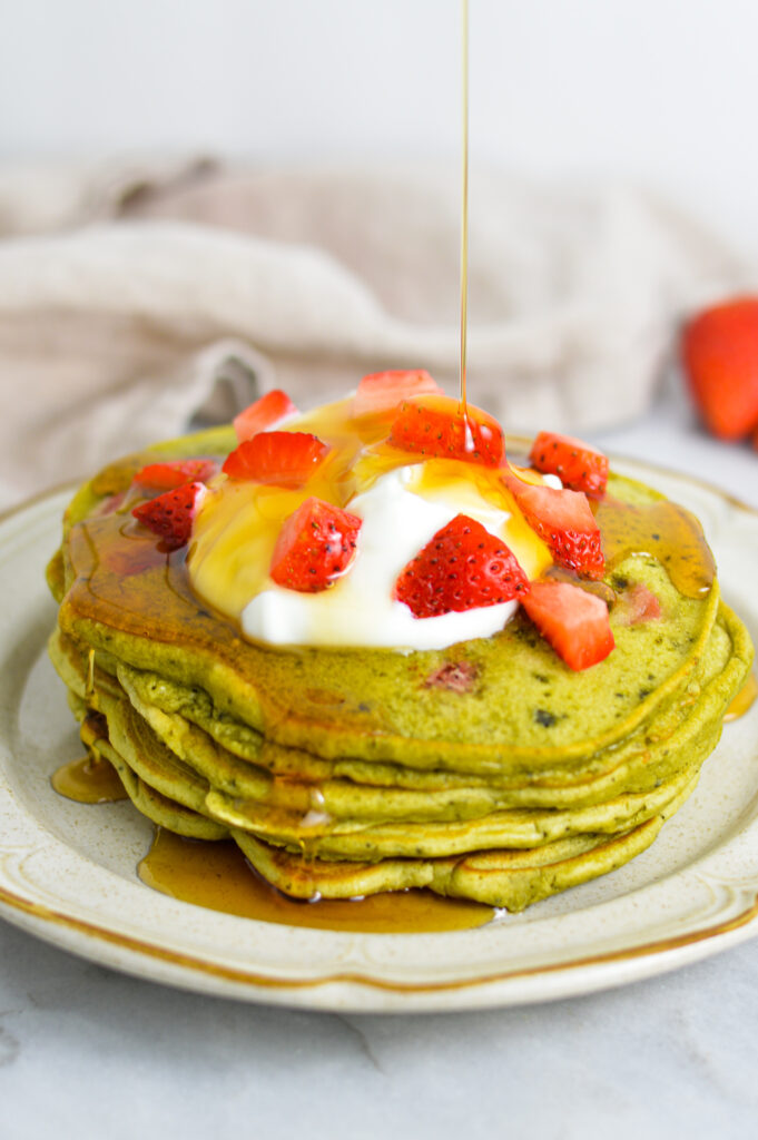 Maple syrup being poured on top of a stack of Strawberry Matcha Pancakes.