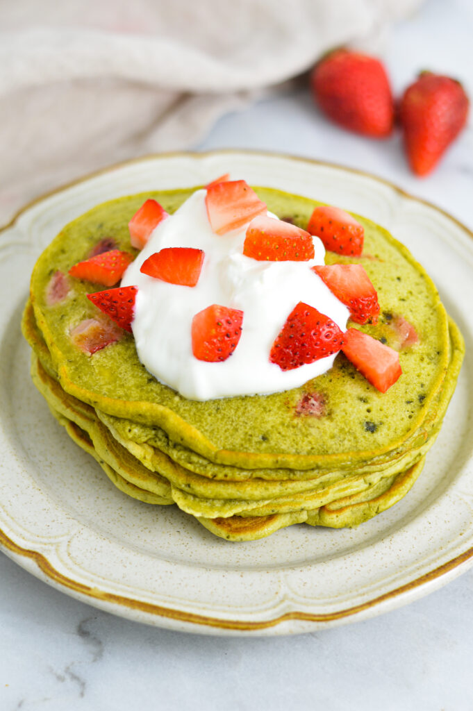 A stack of Strawberry Matcha Pancakes with yogurt and diced strawberries on top.