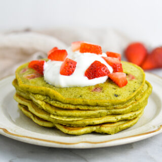 A small stack of Strawberry Matcha Pancakes topped with yogurt and fresh strawberries.