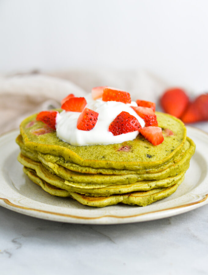 A small stack of Strawberry Matcha Pancakes topped with yogurt and fresh strawberries.