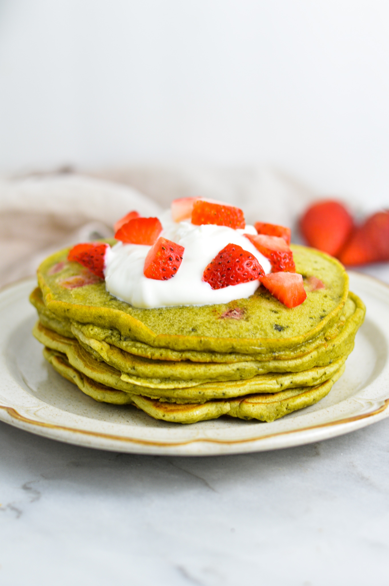 A small stack of Strawberry Matcha Pancakes topped with yogurt and fresh strawberries.