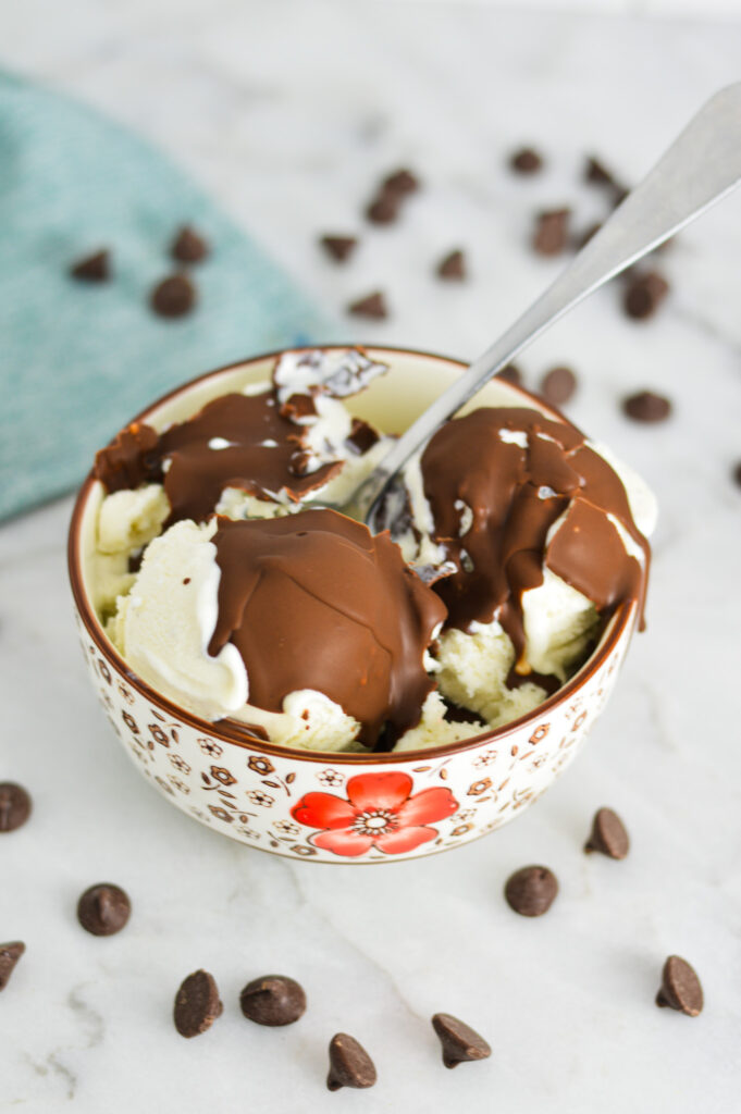 Vegan Magic Shell on top of vanilla ice cream with a spoon breaking through the chocolate.