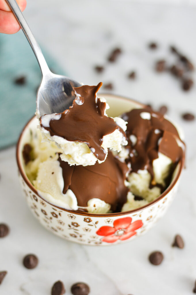 A spoon scooping some Vegan Magic Shell and white ice cream from a bowl.