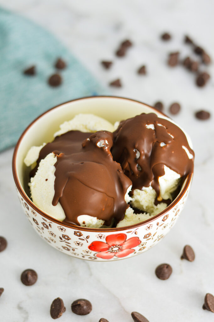 Vegan Magic Shell on top of French vanilla ice cream with semi sweet chocolate chips in the background.