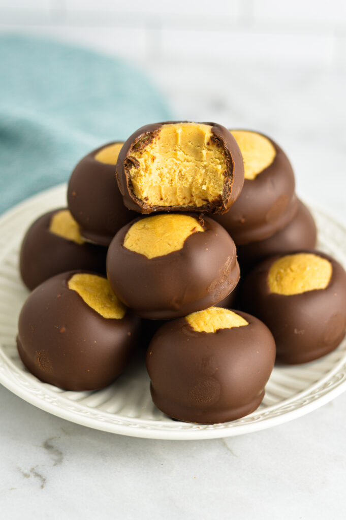 Buckeyes peanut butter chocolate balls on a small plate with a bite taken out of one of the fudge balls.