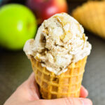 A hand holding No Churn Apple Cinnamon Ice Cream in a waffle cone.