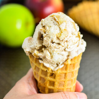 A hand holding No Churn Apple Cinnamon Ice Cream in a waffle cone.