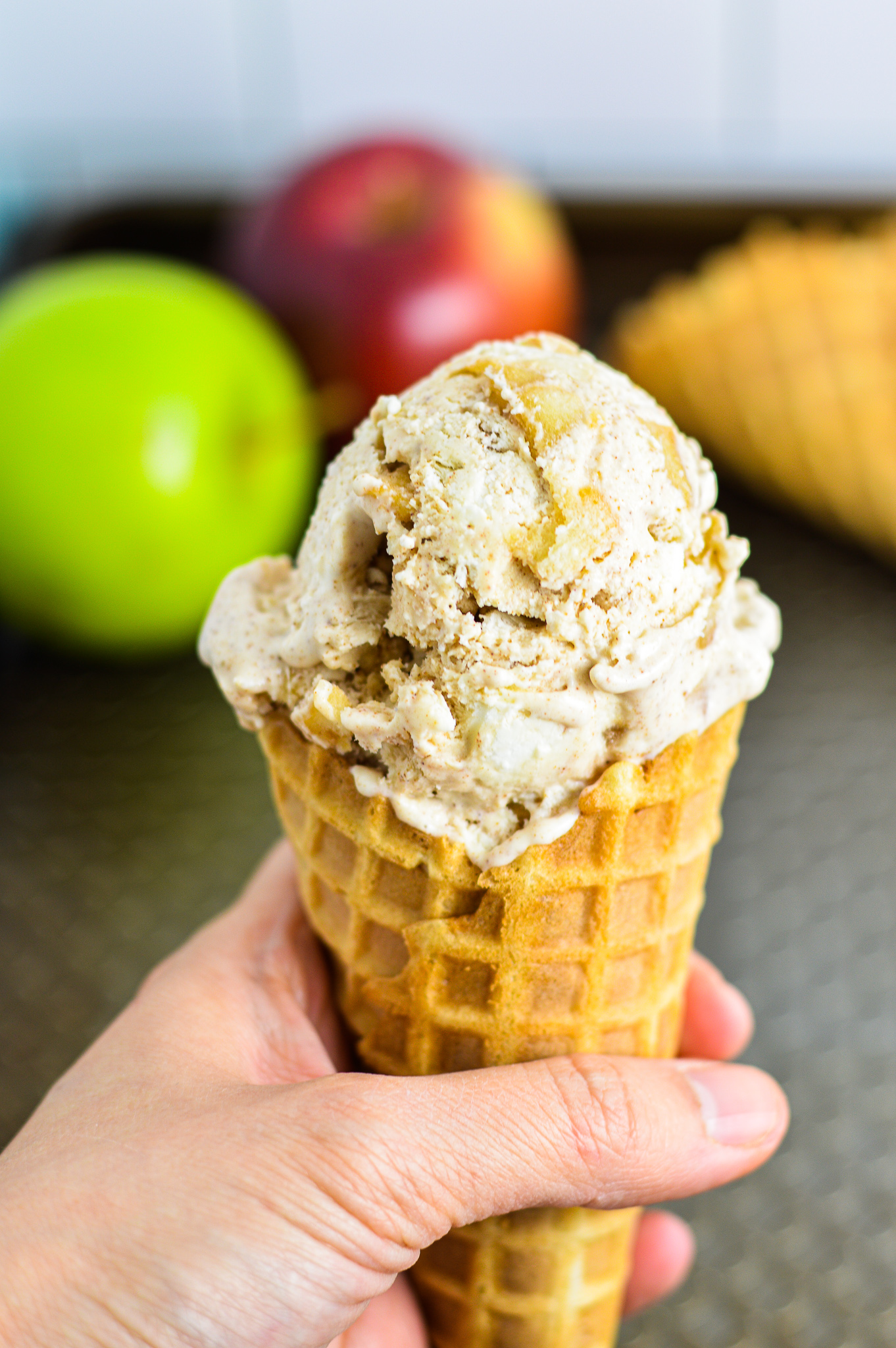 A hand holding No Churn Apple Cinnamon Ice Cream in a waffle cone.