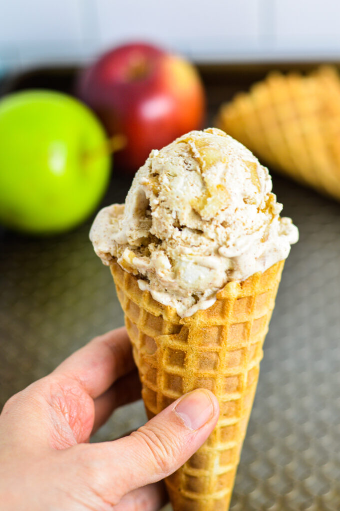 No Churn Apple Cinnamon Ice Cream in a waffle cone with green and red apples in the background.