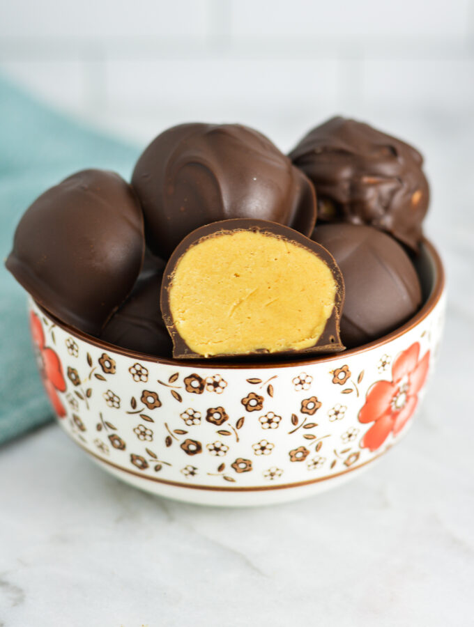 A small bowl filled with Peanut Butter Truffles, with one of them sliced in half.