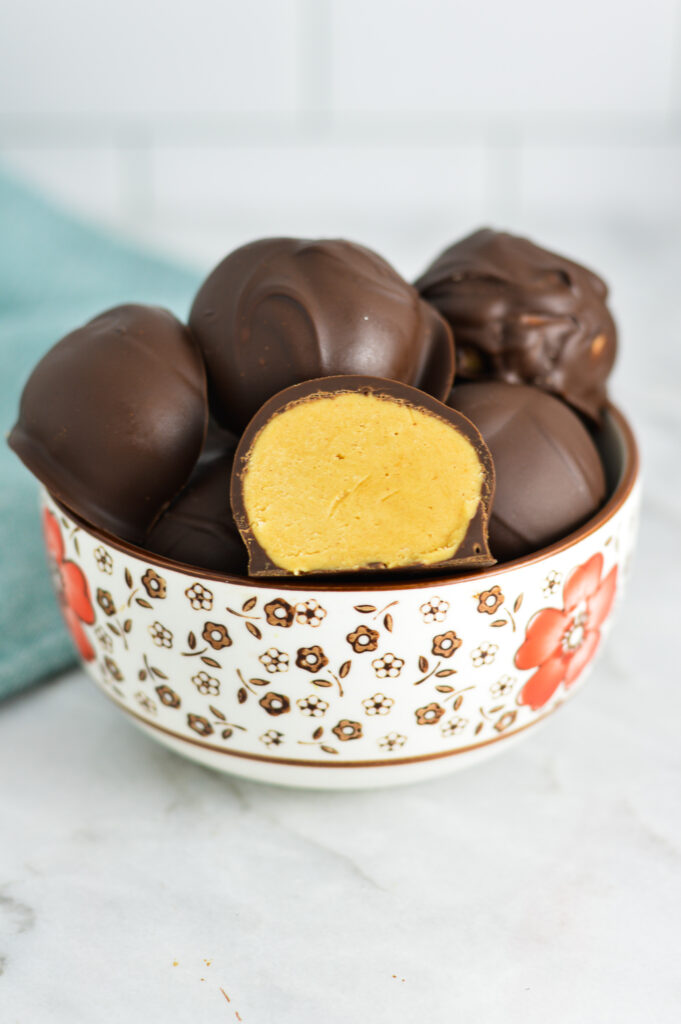 A small bowl filled with Peanut Butter Truffles, with one of them sliced in half.