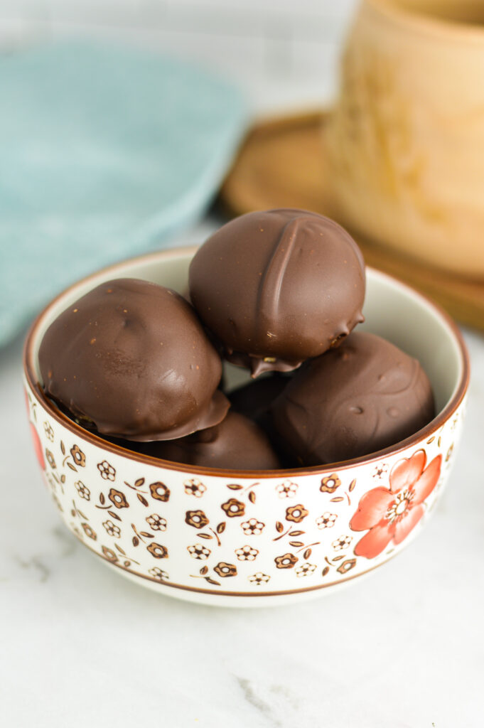 A small bowl filled with Peanut Butter Truffles with a large mug in the background.