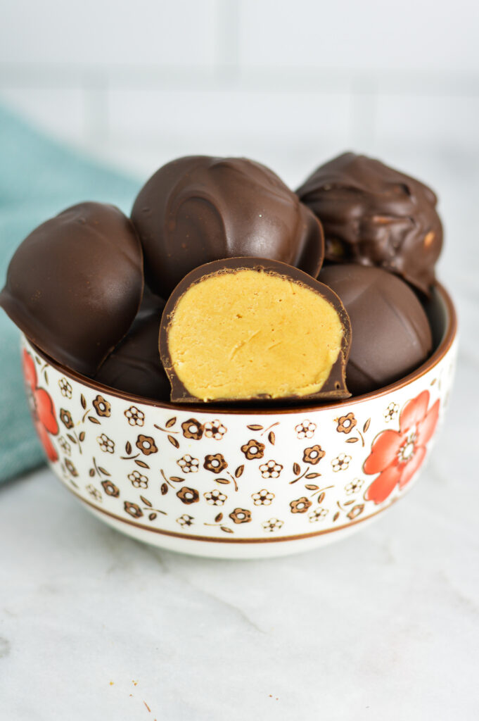 A bowl of Peanut Butter Truffles with one of them cut to show the peanut butter fudge center.