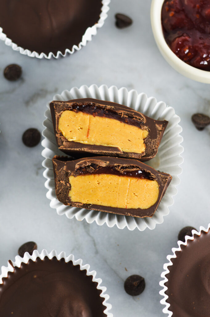 Peanut butter and jam chocolate cups in a muffin cup with a small container of jam in the background.