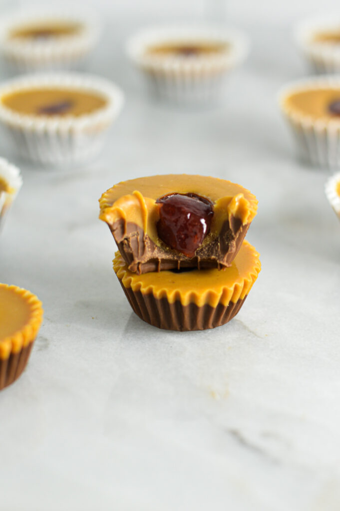 Two Peanut Butter and Jelly Nutella Cups with the mini paper liners taken off and a bite taken out of the top cup showing the strawberry jam on the inside.