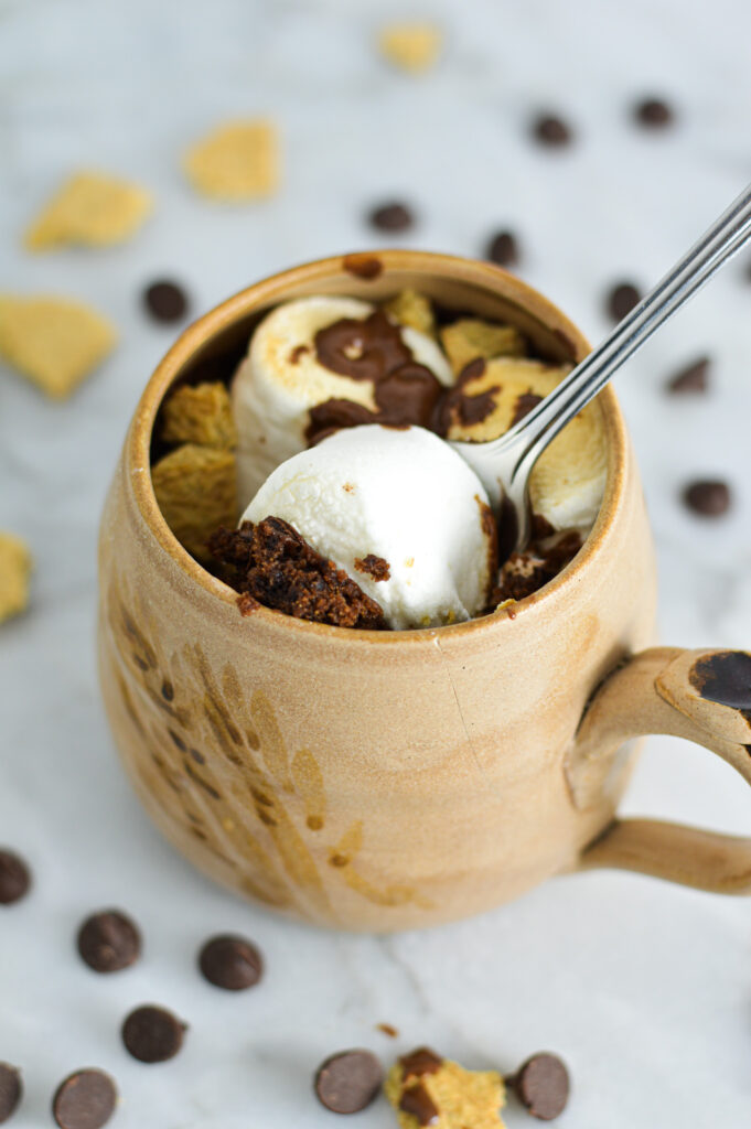 A small silver spoon in a moist S'mores Mug Cake, scooping up the golden brown marshmallow.