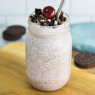 Cherry Oreo Milkshake in a clear glass topped with cookie crumbs and a dark red cherry.