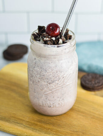 Cherry Oreo Milkshake in a clear glass topped with cookie crumbs and a dark red cherry.