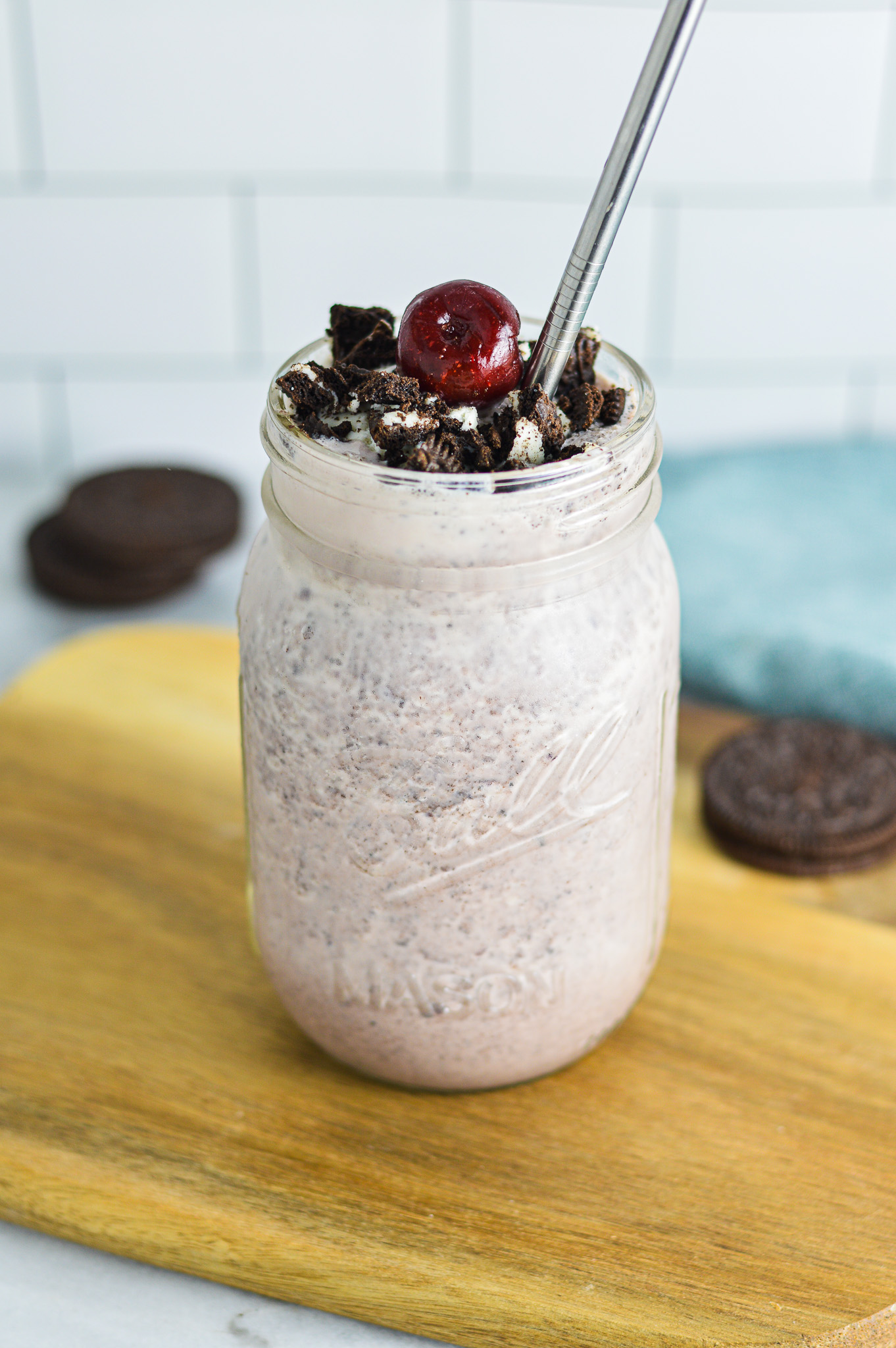 Cherry Oreo Milkshake in a clear glass topped with cookie crumbs and a dark red cherry.