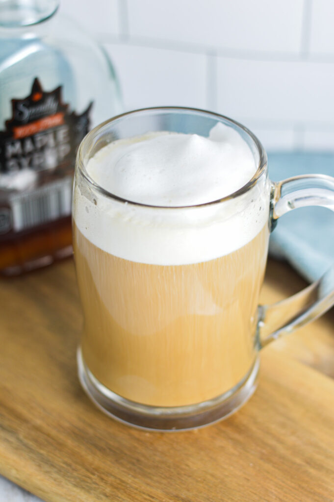 Maple Latte in a glass mug with a jar of maple syrup in the background.