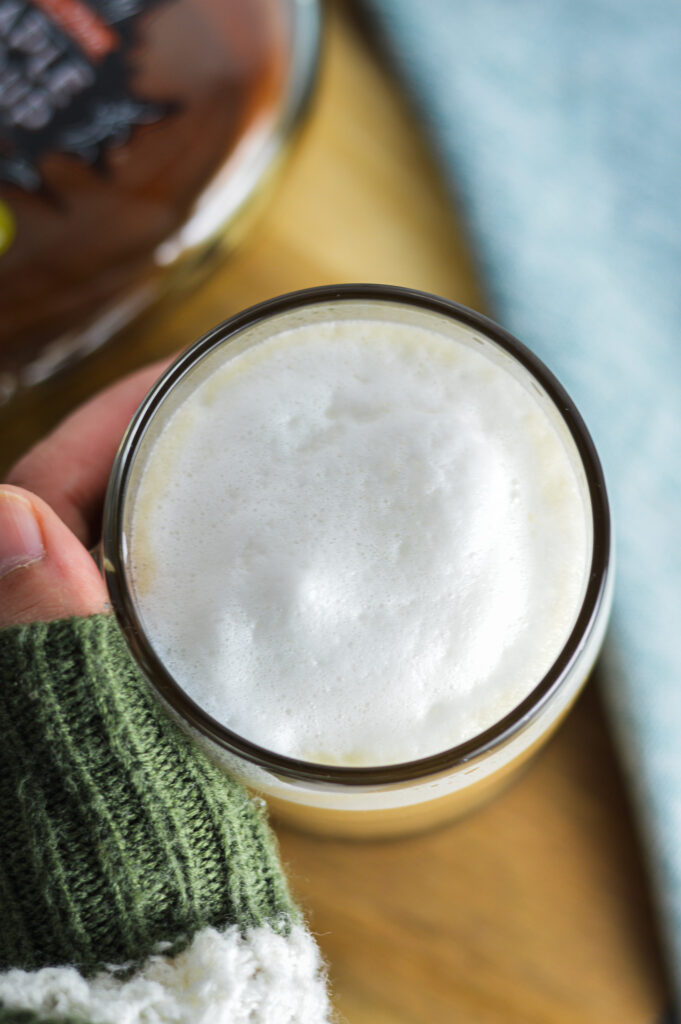 A hand in a cozy sweater holding a mug of Maple Latte.