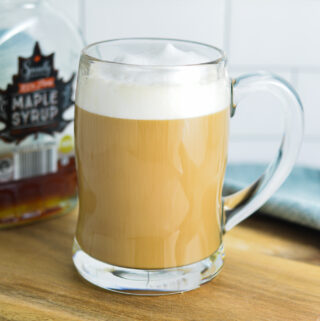 Maple Latte in a glass cup, with a maple syrup container in the background.