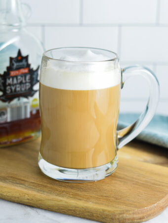 Maple Latte in a glass cup, with a maple syrup container in the background.