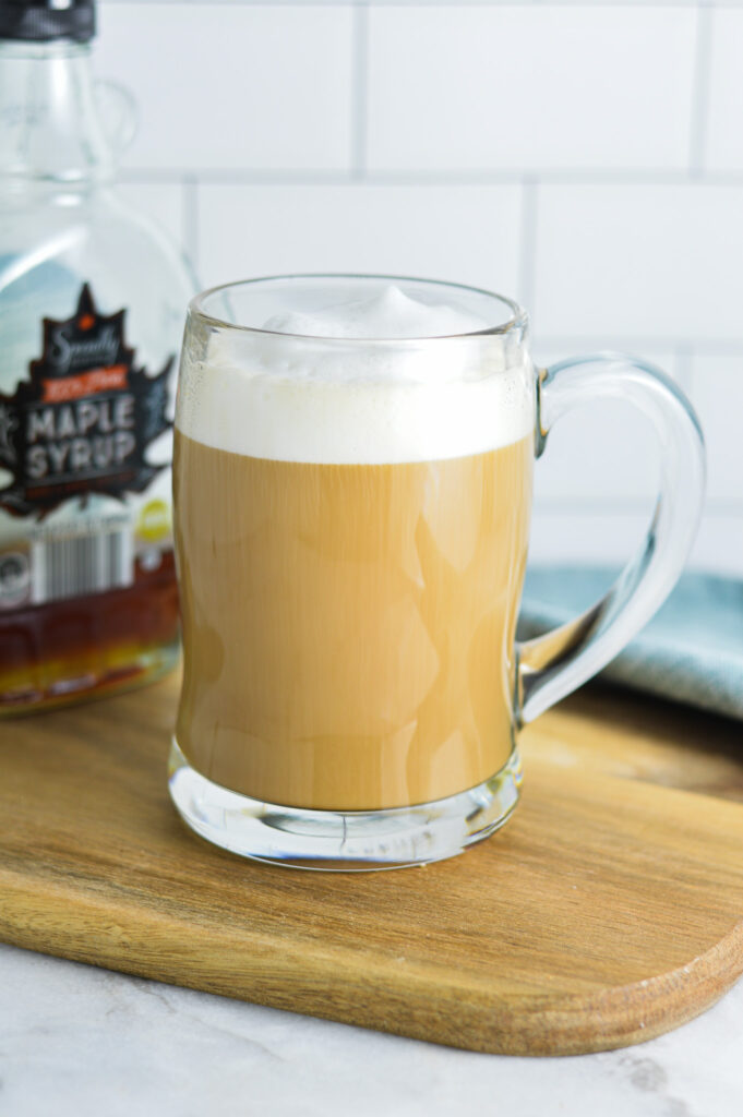 Maple Latte in a glass cup, with a maple syrup container in the background.