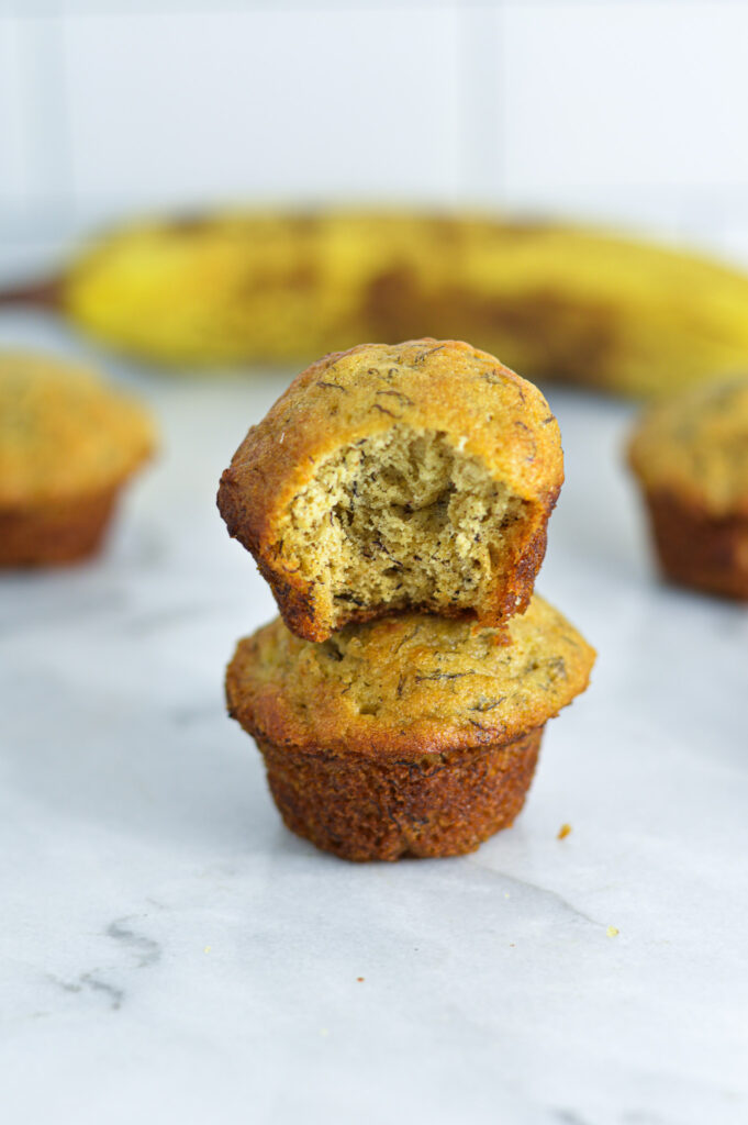 Mini Banana Muffins stacked with a ripe brown banana in the background.