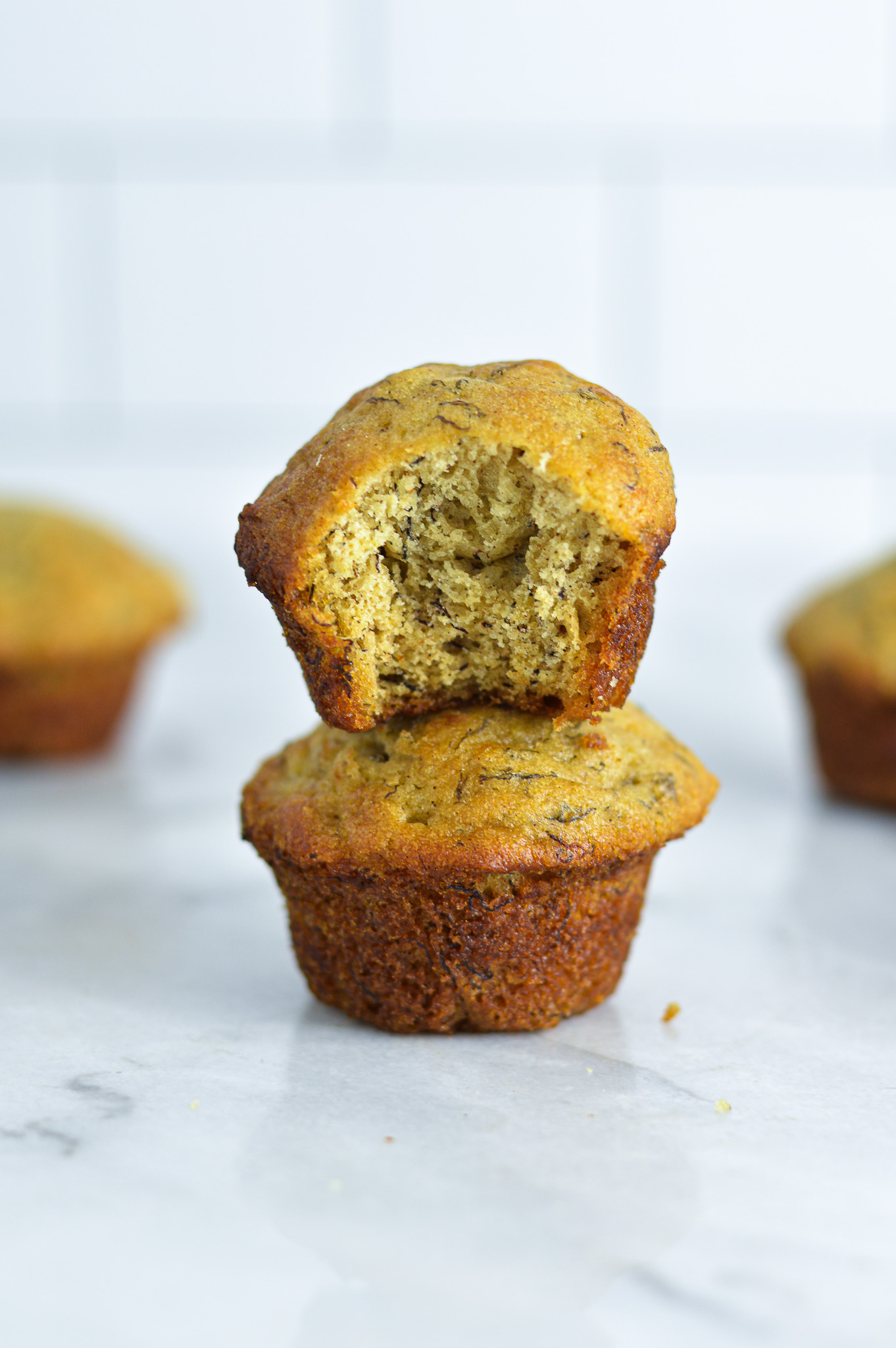 Two Mini Banana Muffins stacked on a white granite surface.