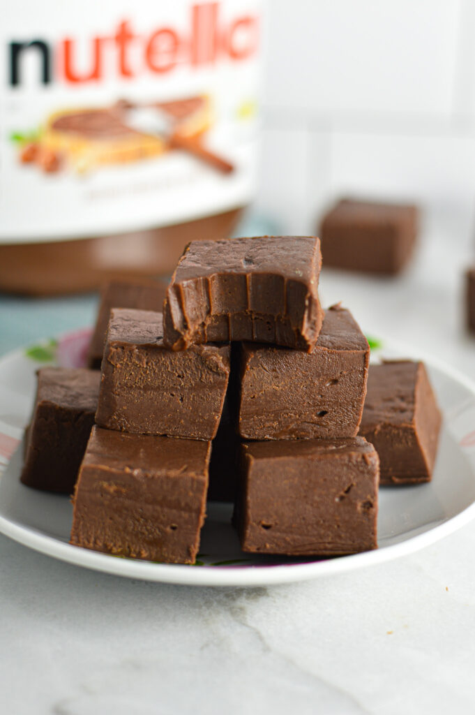 Fudgy Nutella Fudge on top of a plate with a bite taken out of the top piece.