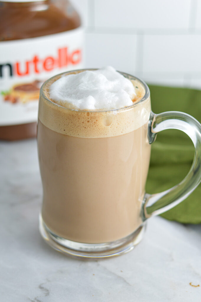 Nutella Latte in a glass mug with foamed milk on top.